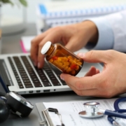 Image of doctor holding a prescription bottle while typing on a computer
