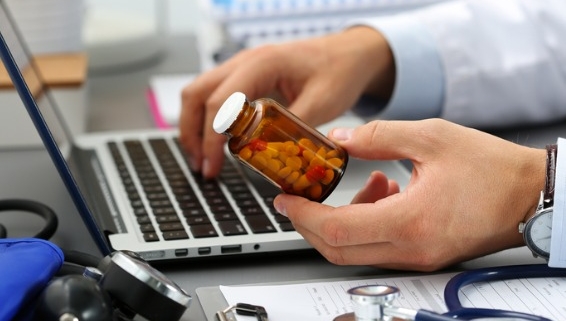 Image of doctor holding a prescription bottle while typing on a computer